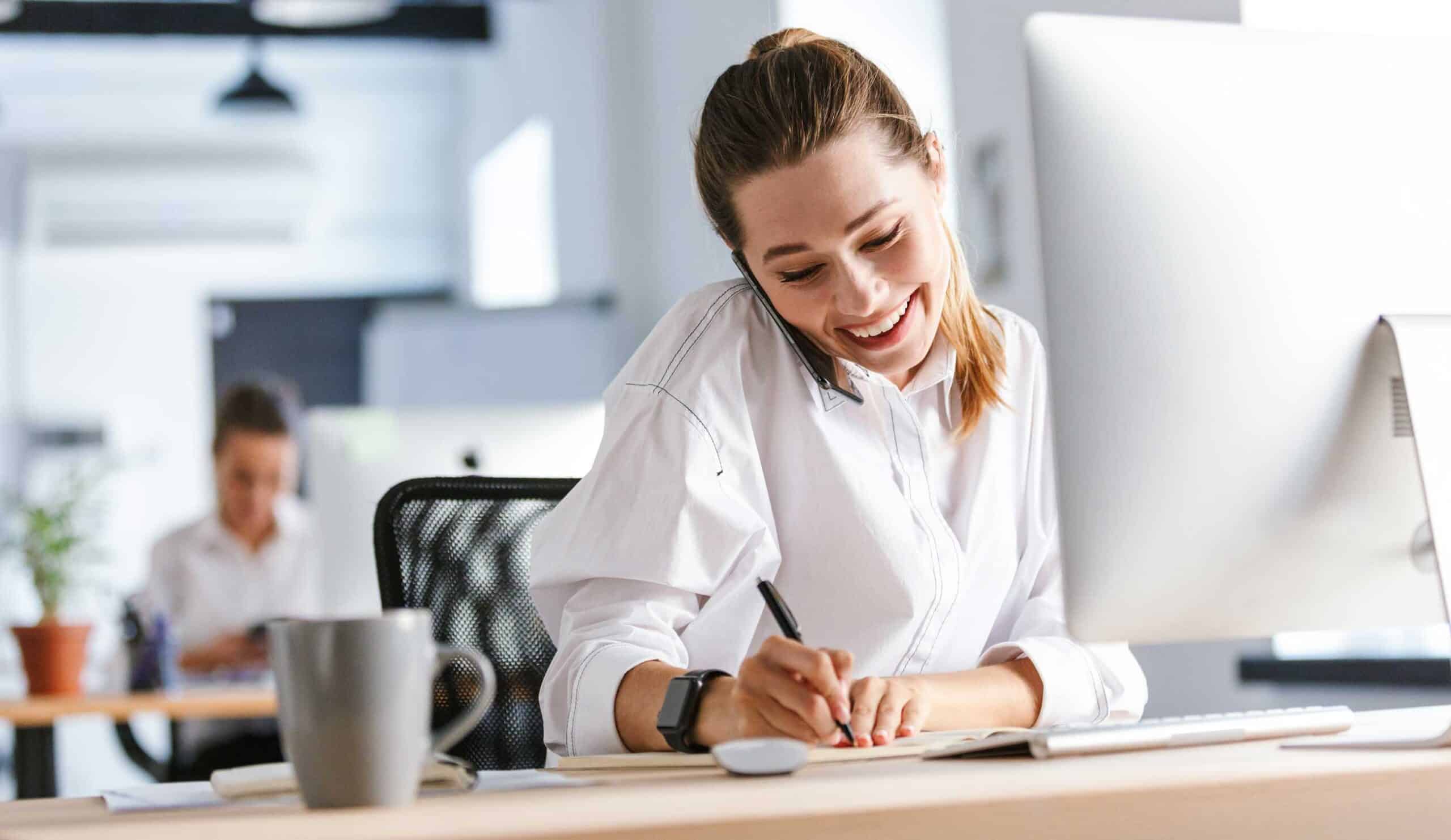 Kontakt, Anfrage, Photovoltaik Mitarbeiterin telefoniert an Schreibtisch und macht dabei Notizen.