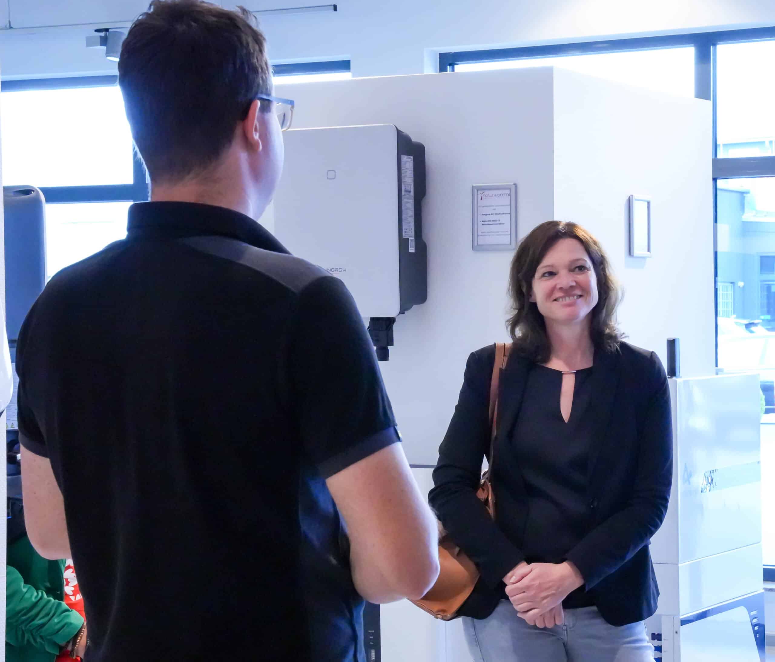 Frau mit braunen Haaren lächelt bei Gespräch mit Mann in der Photovoltaik Ausstellung Bruchköbel.