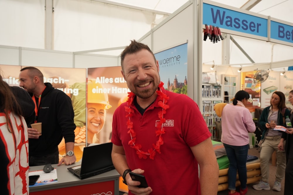 Gewinnspiel Wächtersbach04200 Mann lächelt in Kamera. Im Hintergrund sieht man Messestände