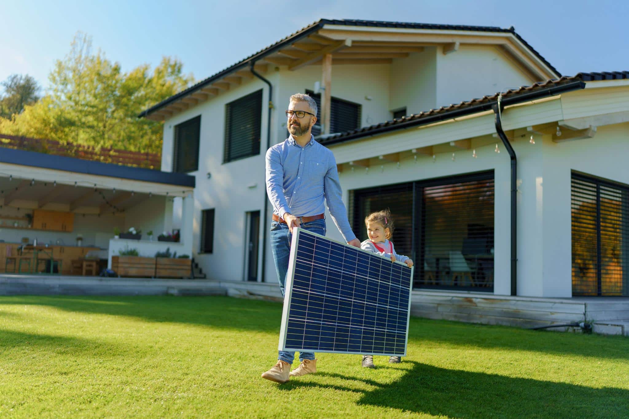 Photovoltaik Komplettanlage Vater und Tochter tragen Solarmodul im Garten