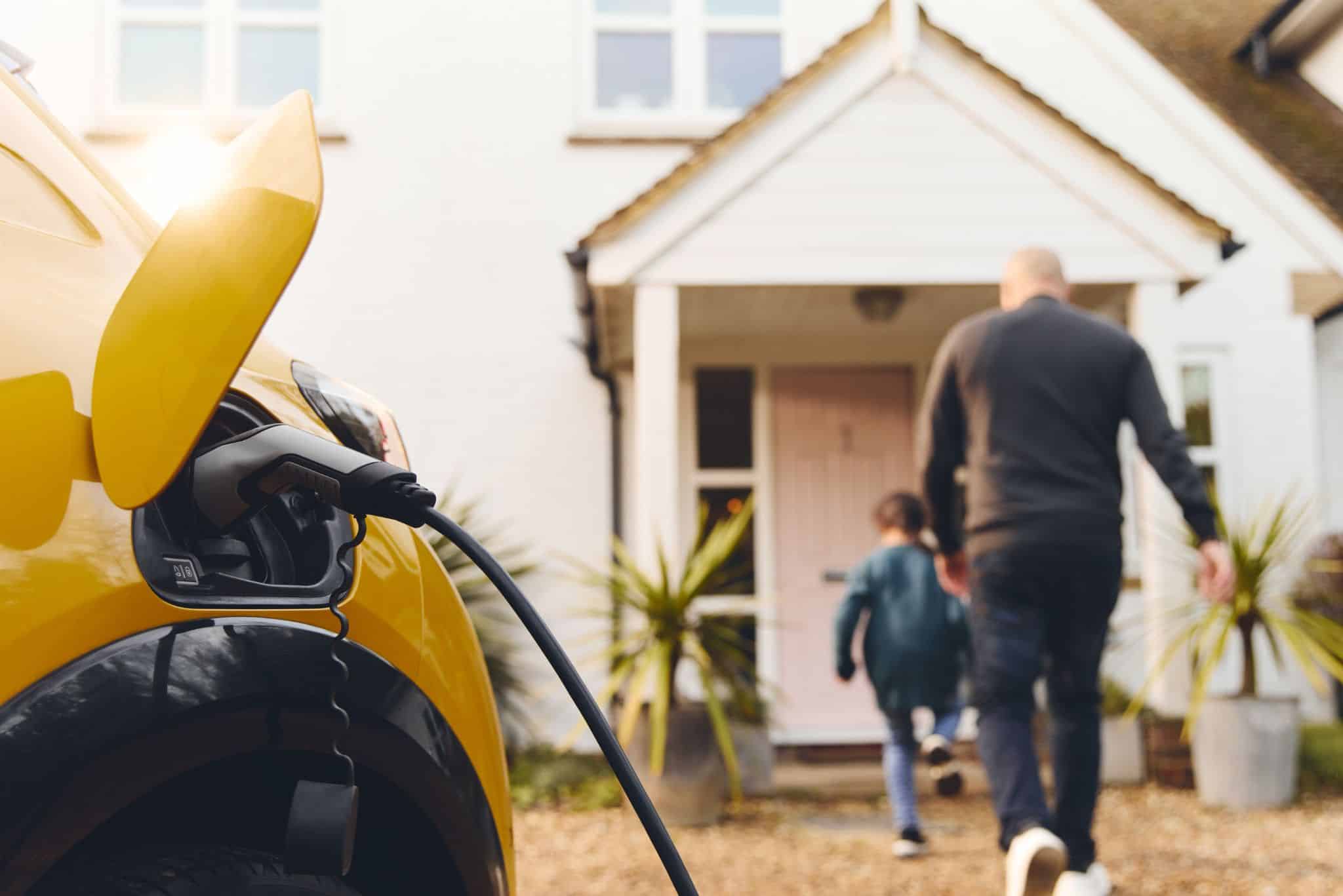 E-Auto steht in Hauseinfahrt, in Hintergrund Eingang